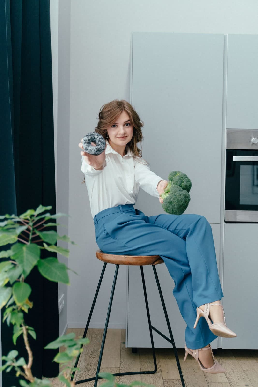 Anna Doran, dietitian, holding a doughnut in one hand and broccoli in the other